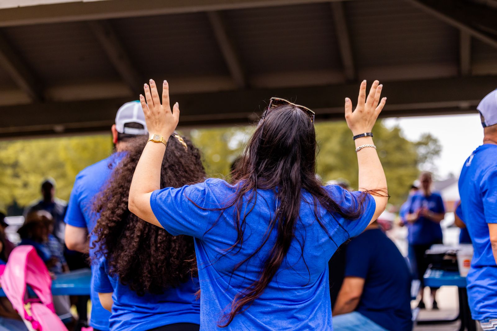 A volunteer raising both hands during an outdoor community gathering.